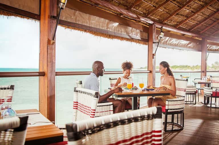 Overwater dining pavilion with three guests enjoying tropical drinks and meals overlooking turquoise lagoon