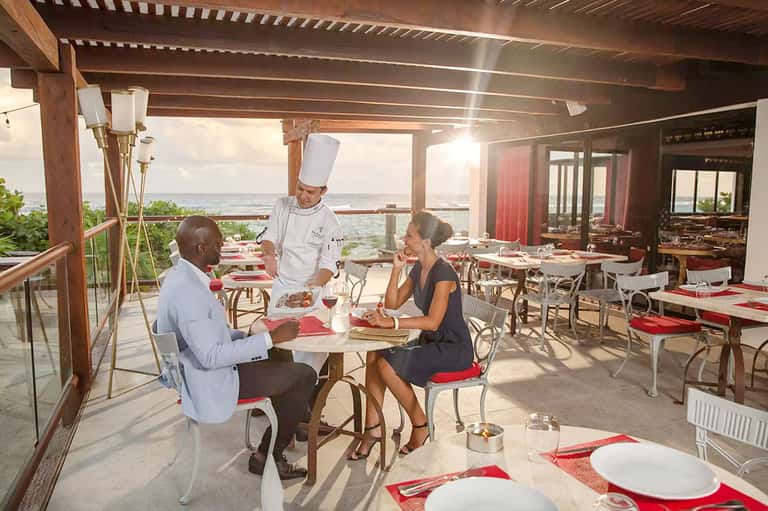 Chef serving dinner to guests on a beachfront terrace restaurant with ocean view