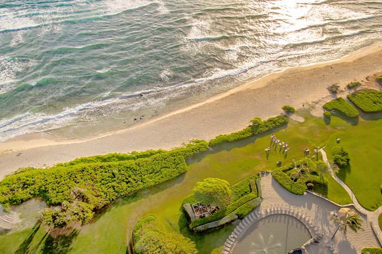Aerial view of manicured beachfront resort grounds with circular structure and ocean waves