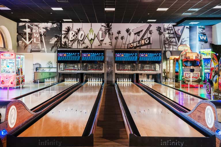 Retro bowling alley with multiple lanes, vintage signage, arcade games, and palm tree decorations