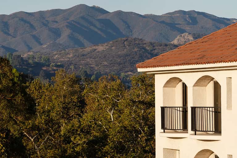 Spanish colonial-style building with arched windows overlooking forested mountains