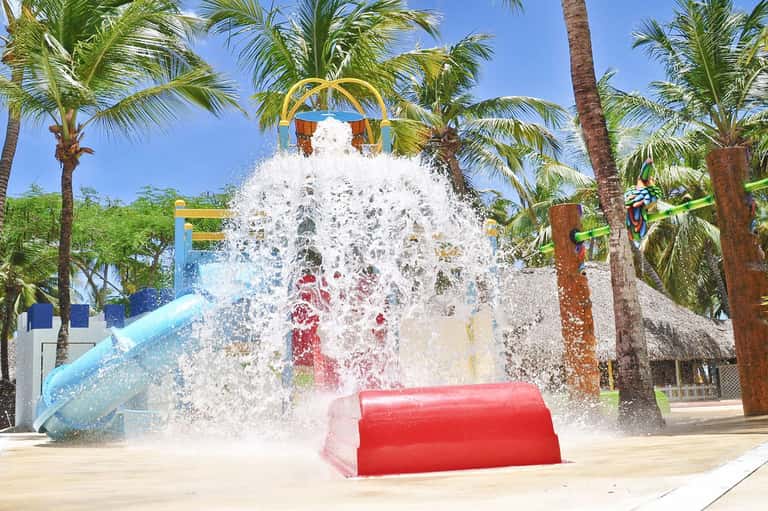 Water bucket dump feature at a tropical water park with palm trees and blue slide