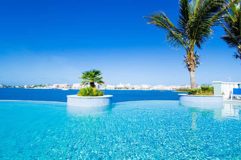Infinity pool with crystalline turquoise water overlooking waterfront cityscape, decorative planters with palm trees