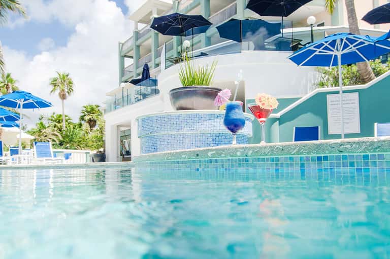 Swimming pool with turquoise water, cocktail drink, palm trees, and modern architecture