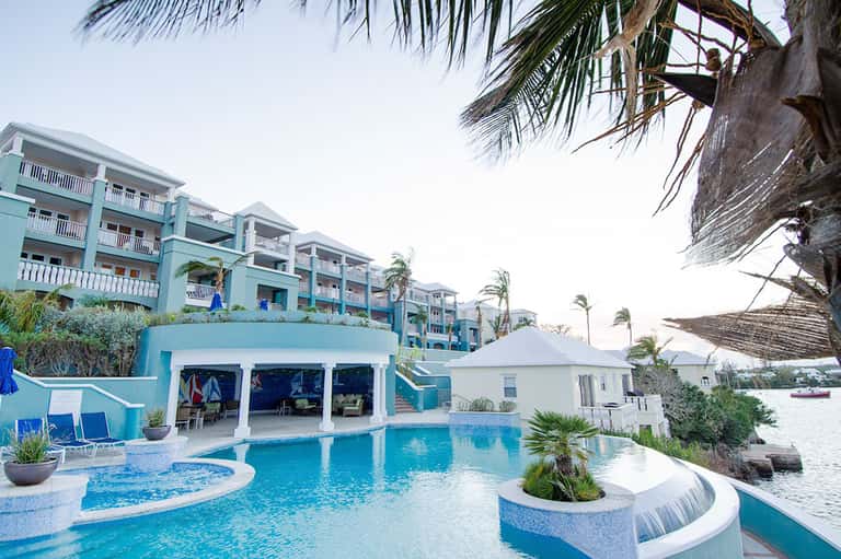 Turquoise resort pool with multi-level design, white cabanas, and palm trees
