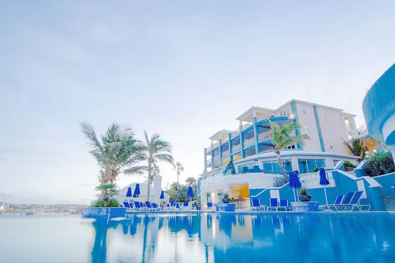 Luxury waterfront resort with blue architecture and palm trees reflecting in still pool water