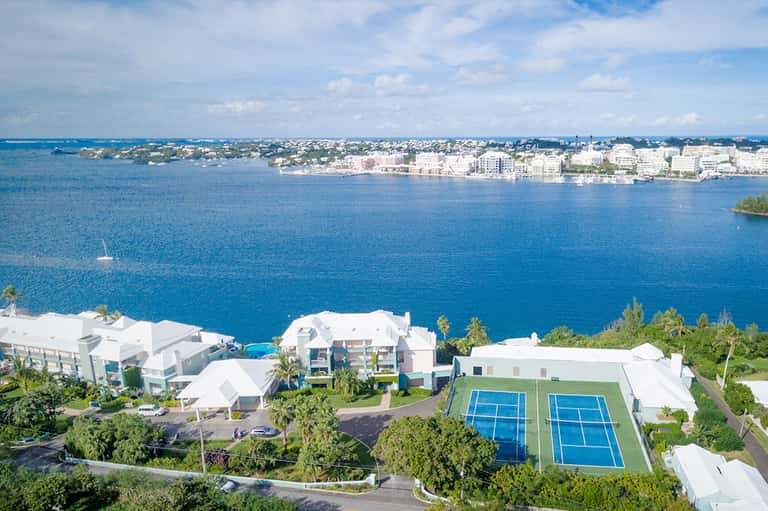 Aerial view of a beachfront resort with white buildings, blue tennis courts, and ocean view
