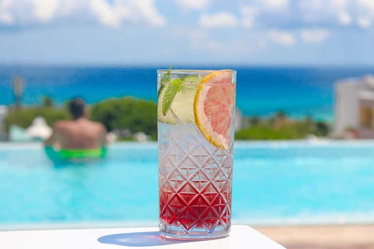 Tropical cocktail with grapefruit and citrus garnish overlooking turquoise ocean and beach