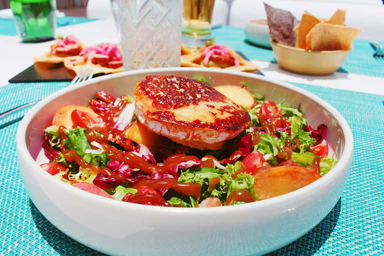 Gourmet salmon dish with colorful salad garnish on turquoise dining table at poolside restaurant