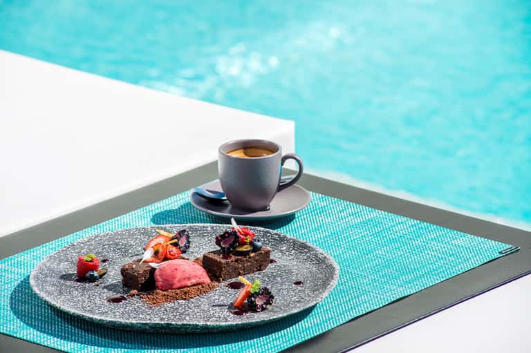 Gourmet chocolate dessert with coffee cup on turquoise placemat overlooking bright blue pool water