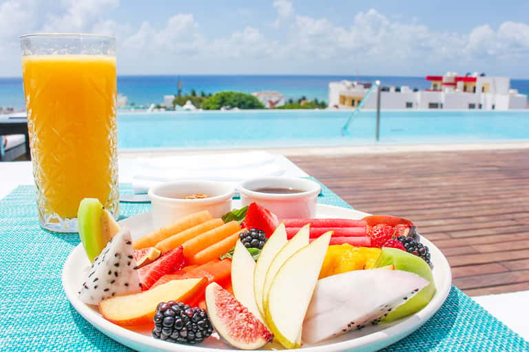 Tropical poolside breakfast with fresh fruit plate, orange juice, and ocean view backdrop
