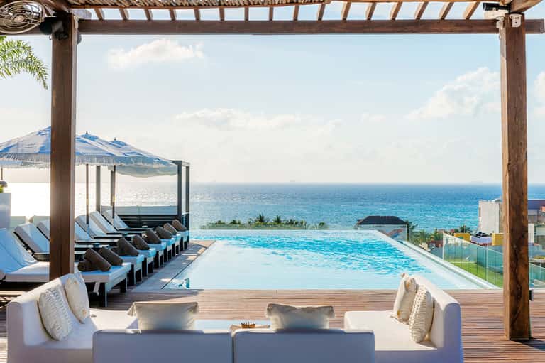 Infinity pool overlooking turquoise ocean with wooden pergola and lounge seating