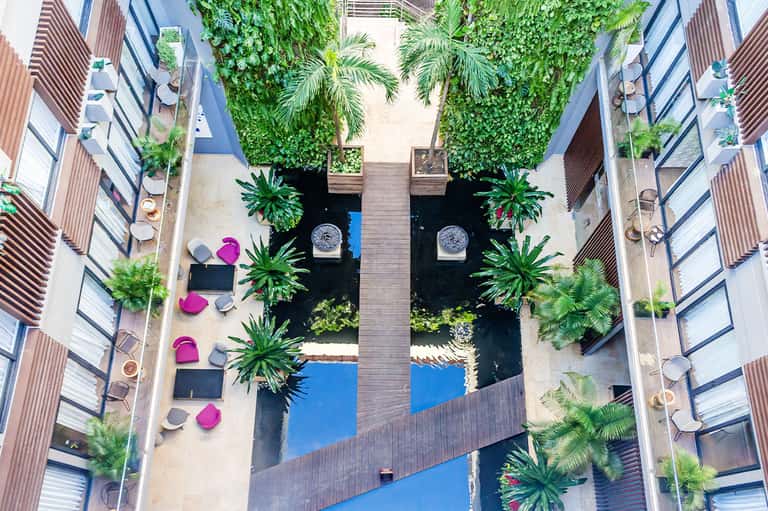 Aerial view of a modern courtyard with pools, tropical plants, and pink umbrellas