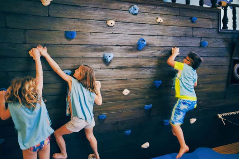 Children climbing wooden wall with colorful holds at indoor play area