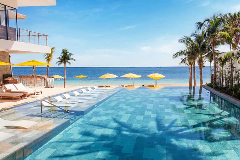 Beachfront infinity pool with yellow umbrellas and ocean views at sunset