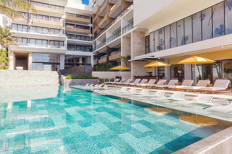 Contemporary resort pool with geometric tile pattern, loungers, yellow umbrellas, and multi-story building