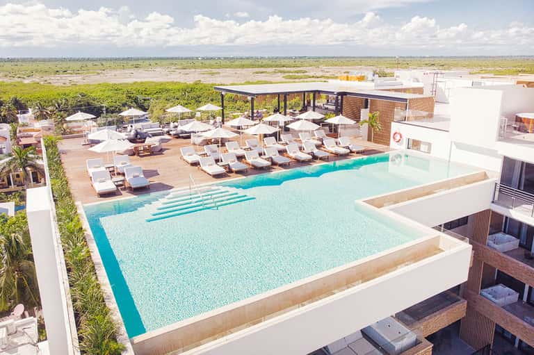 Aerial view of modern resort with turquoise pool, lounge chairs, and flat landscape surroundings
