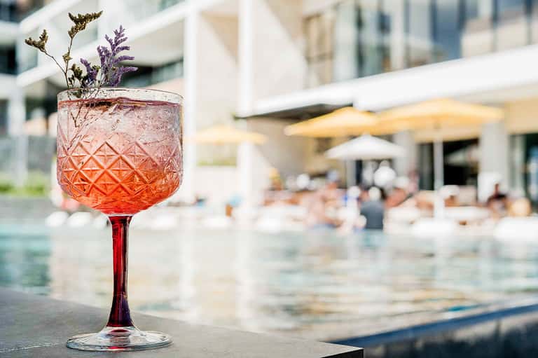Craft cocktail with purple garnish served poolside with blurred resort background