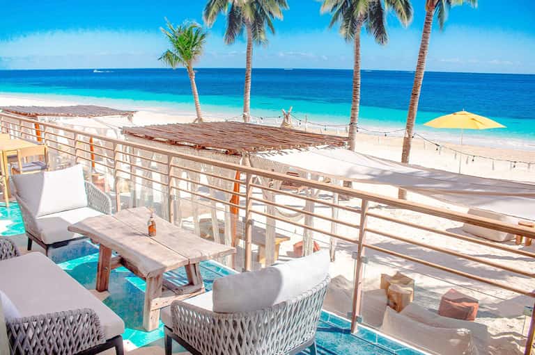 Beach cabana with ocean views, white cushioned seating, and palm trees overhead