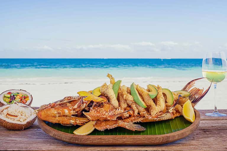 Grilled fish and seafood platter with avocado and lime on wooden table overlooking beach
