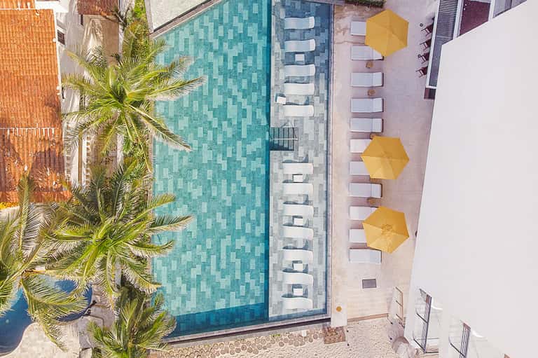 Aerial view of resort pool with turquoise water, white lounge chairs, and yellow umbrellas
