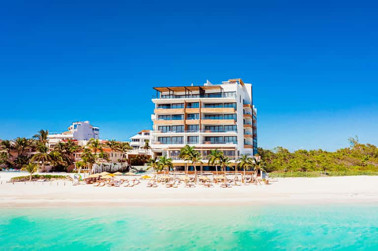 Beachfront resort hotel with white and orange facade, turquoise water, and palm trees