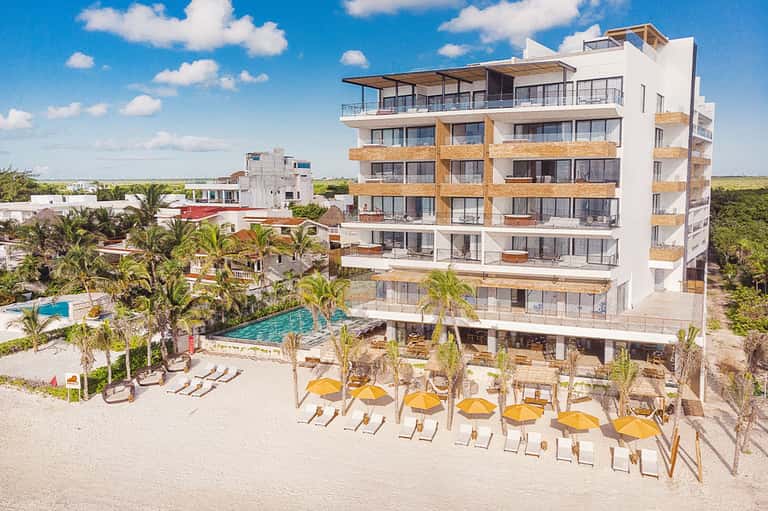 Modern beachfront hotel with yellow umbrellas, lounge chairs, and palm trees