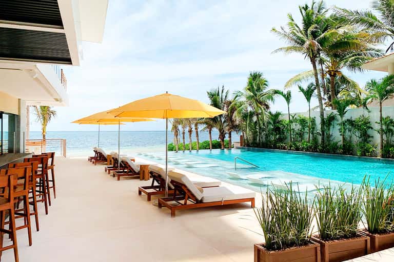 Beachfront infinity pool with lounge chairs, yellow umbrella, and palm trees