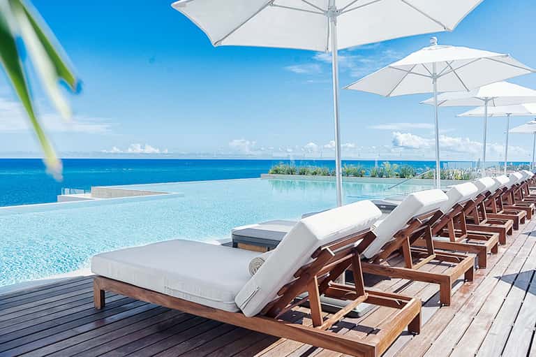 Infinity pool with white umbrellas and wooden lounge chairs overlooking ocean