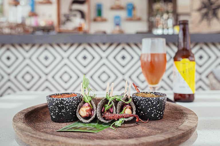 Gourmet appetizers with black sesame-crusted items and fresh garnish beside craft beers