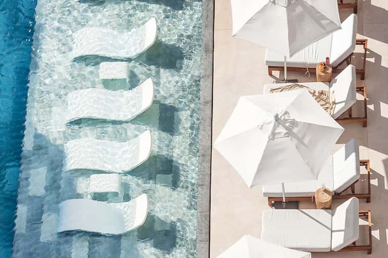 Aerial view of curved pool with lounge chairs, white umbrellas, and pristine water
