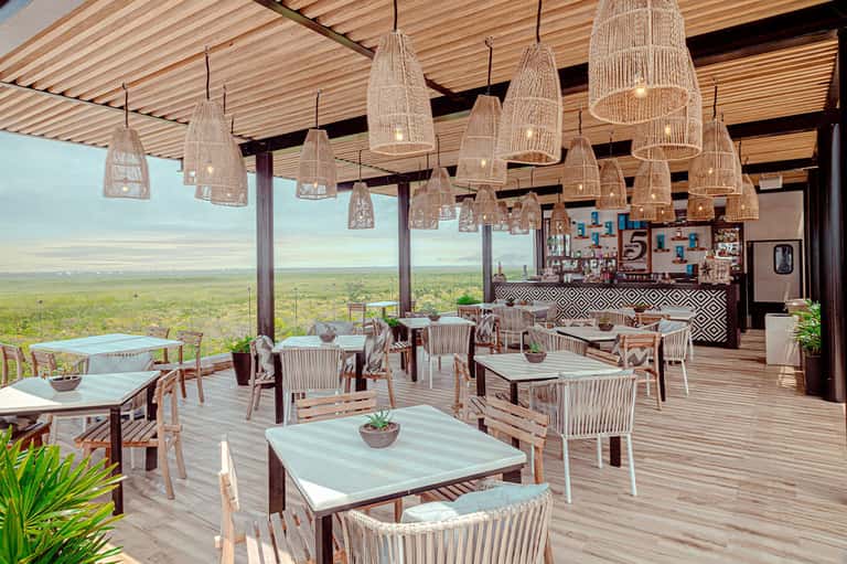 Elevated outdoor dining area with wooden pergola, woven pendant lights, and expansive landscape views