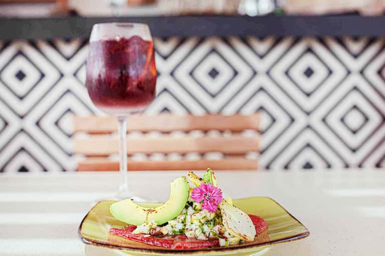 Gourmet plate with avocado and microgreens beside a red wine cocktail