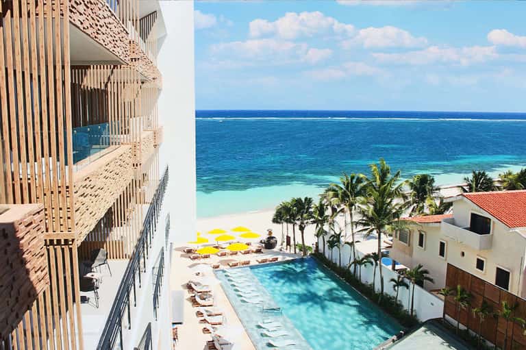 Beachfront resort pool with palm trees overlooking turquoise ocean and white sand beach