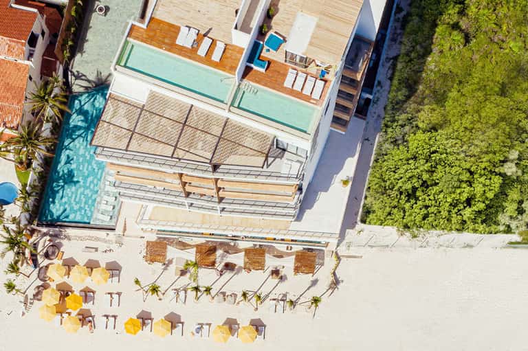 Aerial view of beachfront resort with pools, wooden decks, and umbrellas on sand
