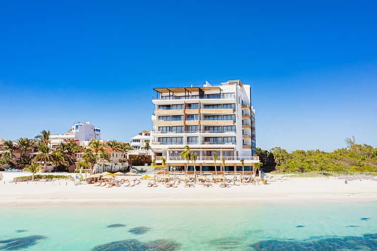 Beachfront hotel with multi-story white building and sandy beach with loungers