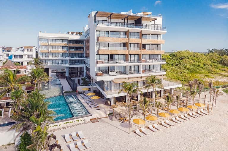 Beachfront hotel exterior with pool, lounge chairs, umbrellas, and sandy beach access