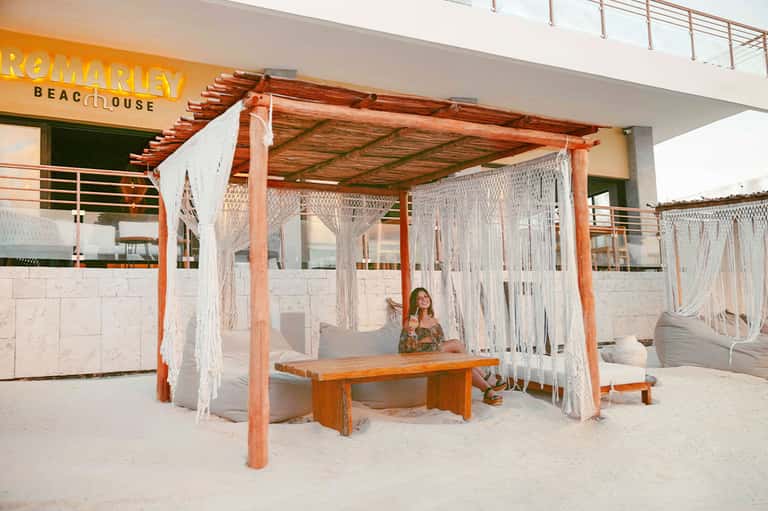 Beachfront cabana with wooden frame, white curtains, and cushioned seating
