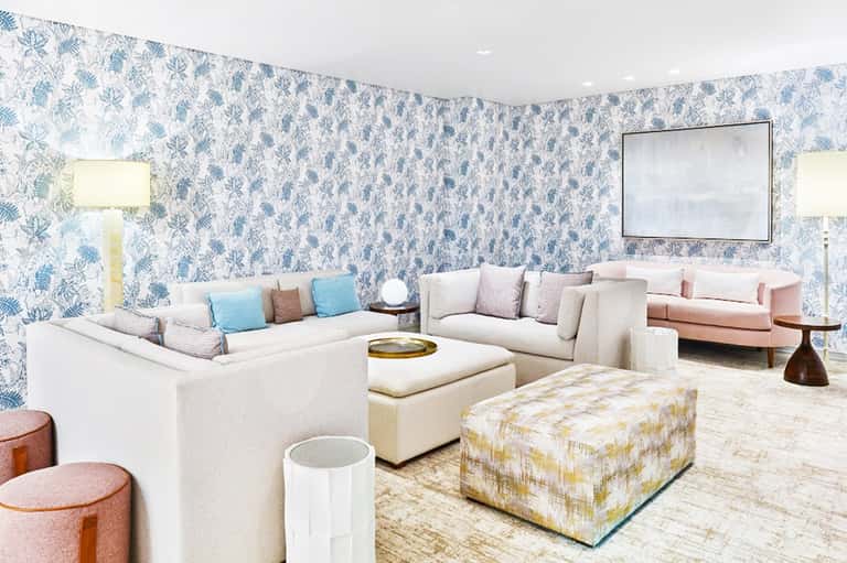Elegant lounge with blue botanical wallpaper, cream seating arrangements, and decorative poufs with neutral tones