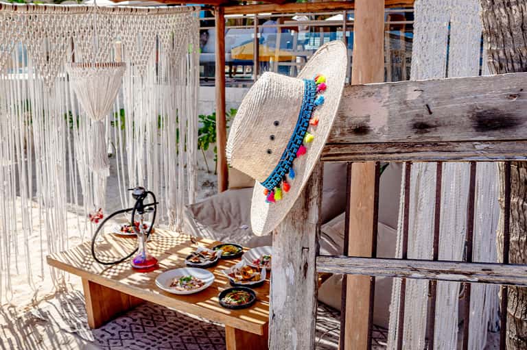 Decorated straw hat on wooden railing overlooking beachfront dining setup