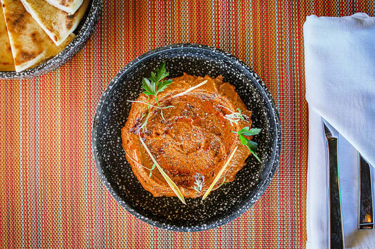 Gourmet dish with orange sauce and fresh herbs served in black speckled bowl on textured placemat