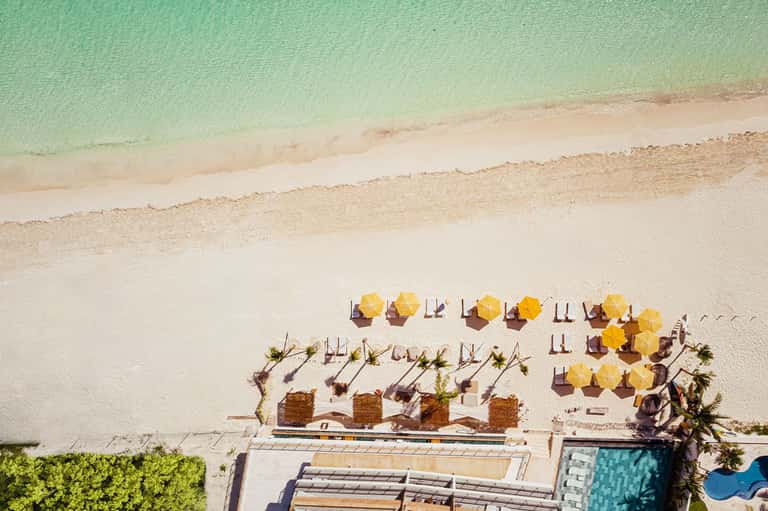 Aerial view of beach resort with yellow umbrellas, loungers, and turquoise ocean