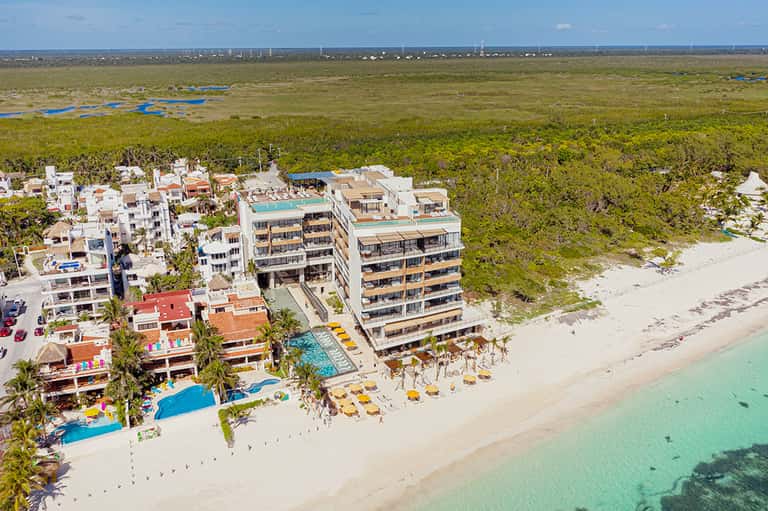Aerial view of beachfront resort with pools, white buildings, and turquoise Caribbean waters surrounded by mangroves