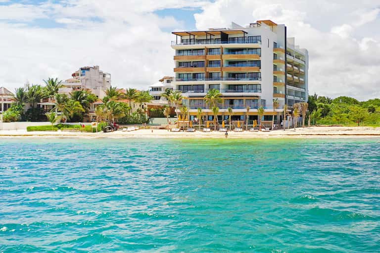 Beachfront resort building with yellow and white exterior overlooking turquoise ocean