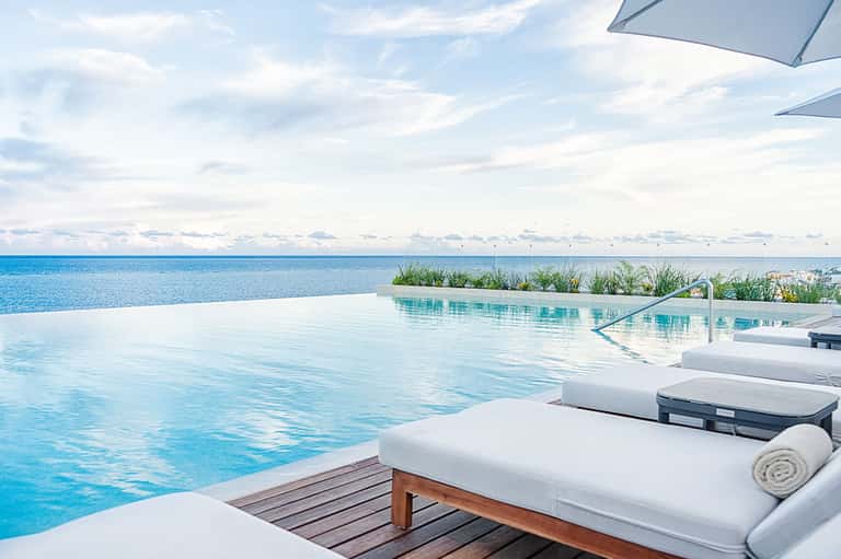 Infinity pool overlooking turquoise ocean with white lounge chairs and umbrellas at beachfront resort