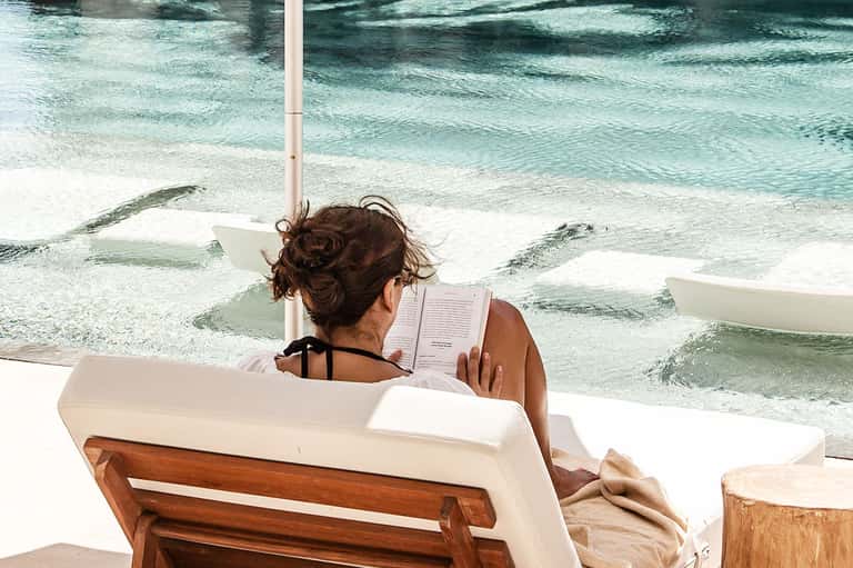Woman reading a book while relaxing on a beach lounge chair with ocean waves in the background