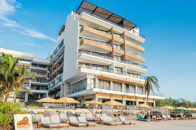 Contemporary beachfront hotel with white and wooden facade, yellow beach umbrellas, and lounging area on sandy shore