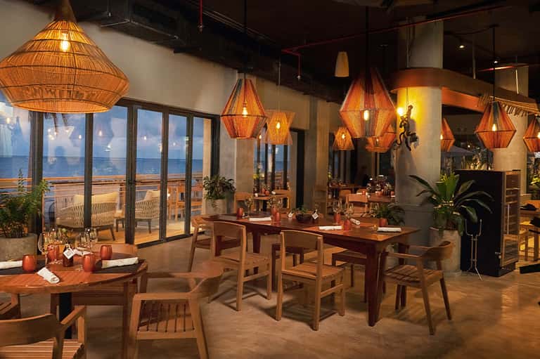 Upscale restaurant interior with woven pendant lights, wooden tables, and ocean views