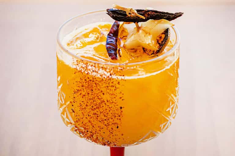 Spiced cocktail with dried chili pepper and vanilla pod garnish in a rocks glass