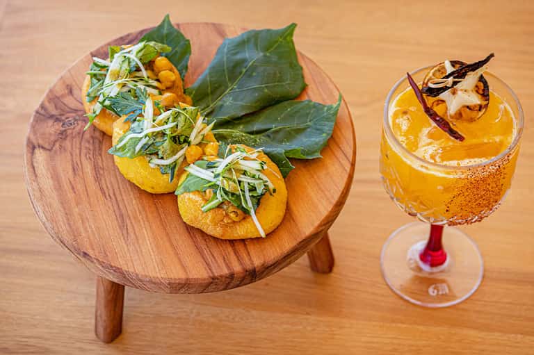Golden tacos with greens on wooden board next to an amber cocktail with spiced rim